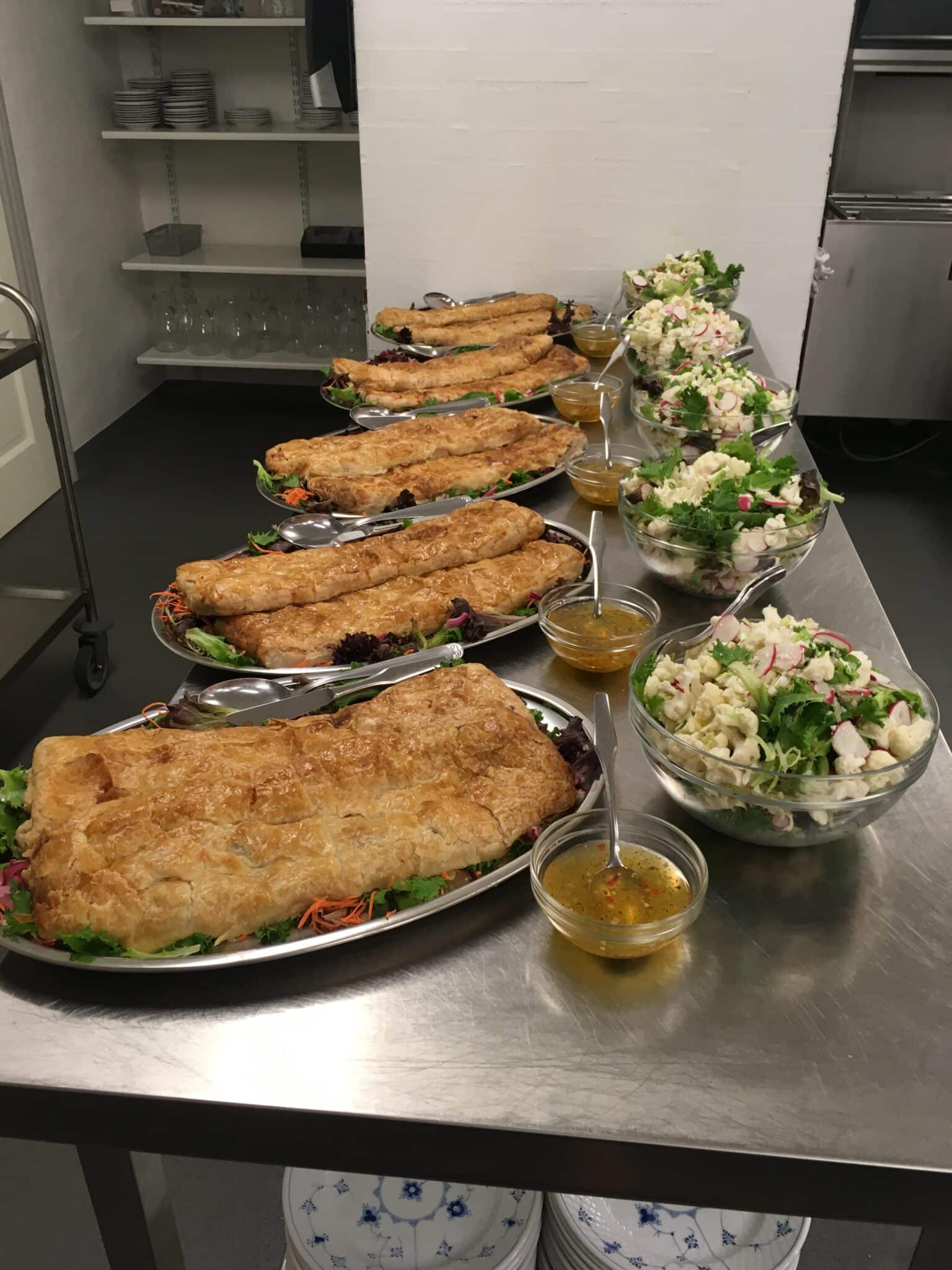 Buffet med tærter, salater og dressing på køkkenbord.
